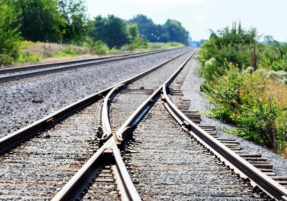 Two railroad tracks merging into one, used as a metaphor for a business merger.