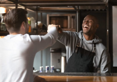 Laughing,African,American,Barista,Fists,Bumping,With,Customer,In,Cafe,
