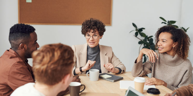 A group of happy and excited professionals sit around a desk.